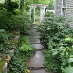 Single broken bluestone steppers draw the eye to the arbor at the far end of the path